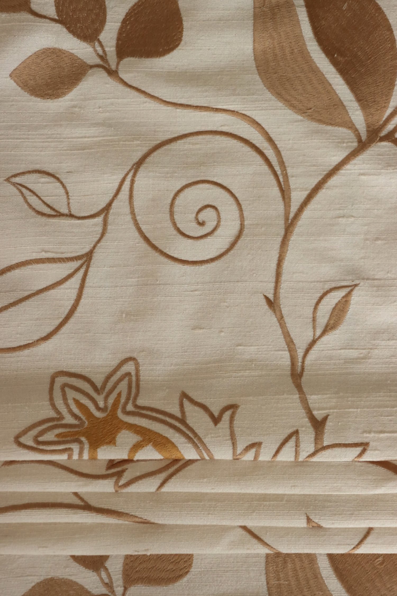 MOREEN CAMEL silk fabric by Arte Fresca Outlet, folded precisely like a Roman blind, highlighting its structured yet soft nature, the clear definition of its embroidered floral pattern, and its ability to create sophisticated, richly textured window coverings.