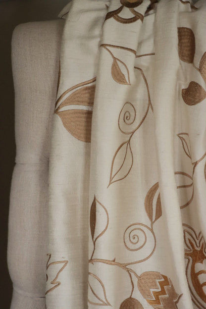 MOREEN CAMEL silk fabric by Arte Fresca Outlet draped loosely over a light upholstered chair back, illustrating the elegant scale of its embroidered floral pattern in brown on camel, ideal for assessing design repeat and luxurious drape for home decor.
