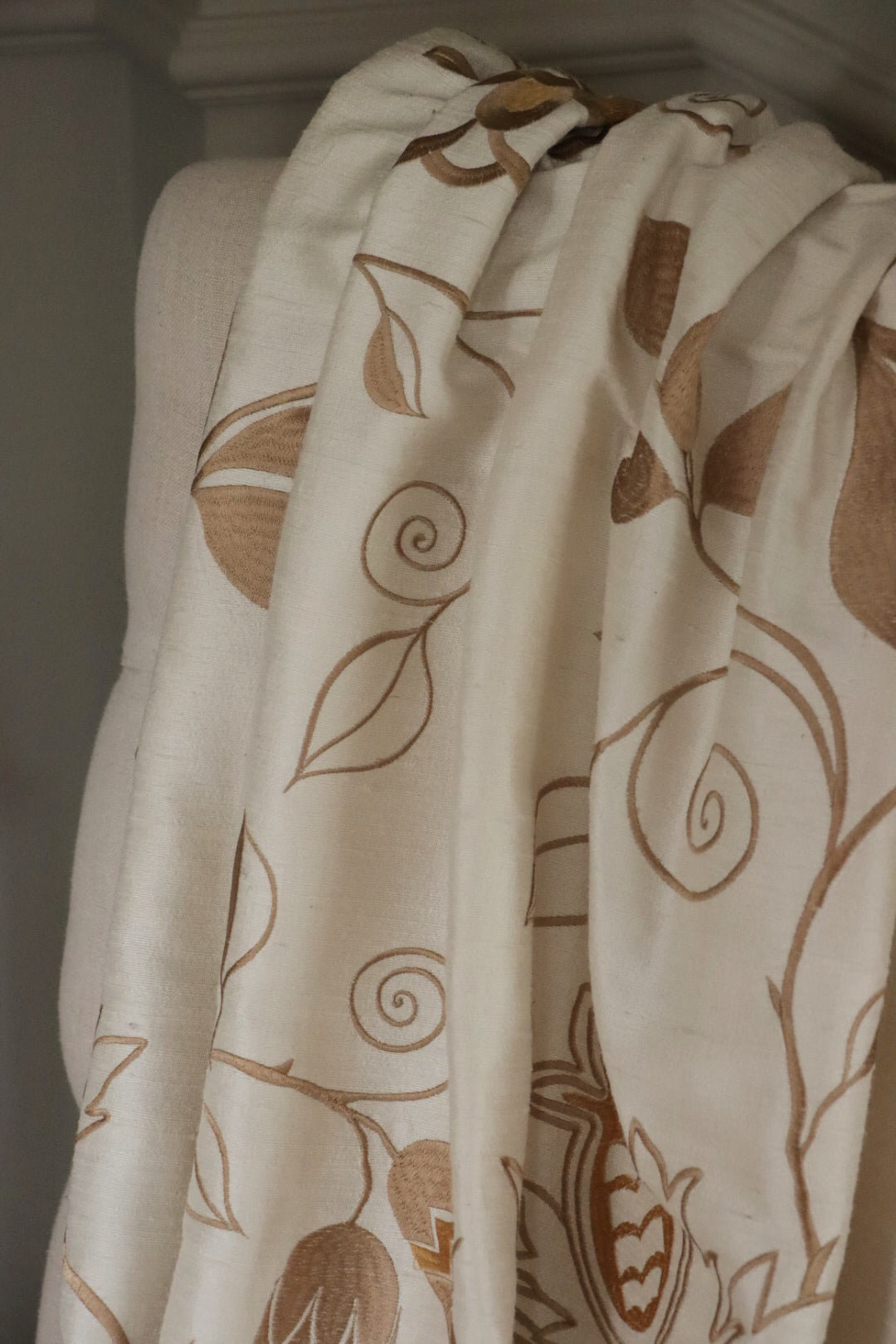 MOREEN CAMEL silk fabric by Arte Fresca Outlet draped loosely over a light upholstered chair back, illustrating the elegant scale of its embroidered floral pattern in brown on camel, ideal for assessing design repeat and luxurious drape for home decor.