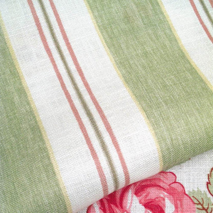 A close-up of striped fabric with vertical bands of sage green, white, and dusty pink, featuring a folded corner that reveals a pink floral print.