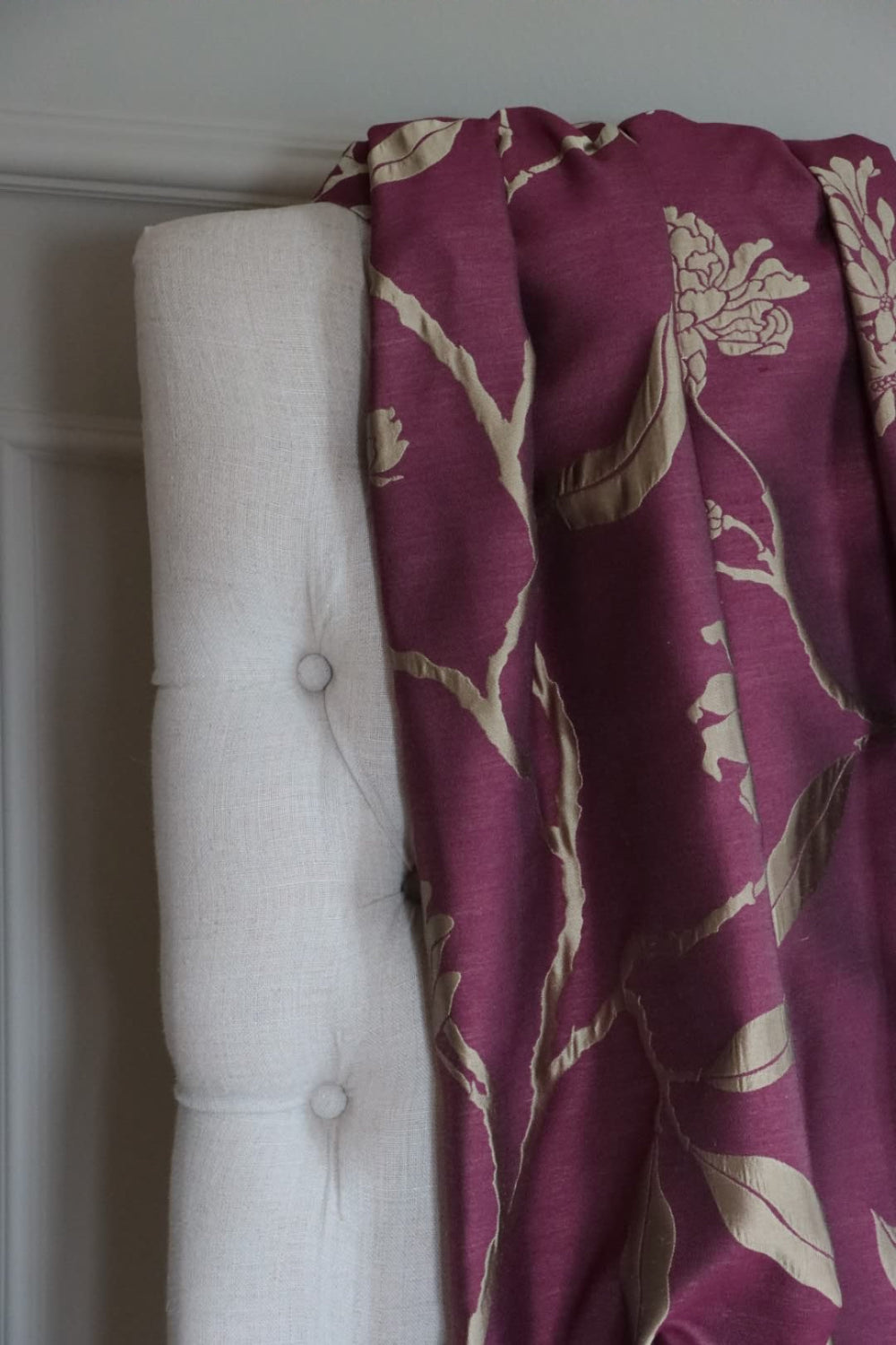 PENCARROW DARK RED silk fabric by Arte Fresca Outlet draped loosely over a light-colored upholstered chair back, illustrating the scale of its large floral pattern with stylized gold-silver flowers on a deep dark red background, showcasing its smooth texture.