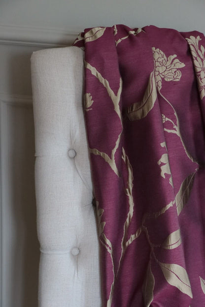 PENCARROW DARK RED silk fabric by Arte Fresca Outlet draped loosely over a light-colored upholstered chair back, illustrating the scale of its large floral pattern with stylized gold-silver flowers on a deep dark red background, showcasing its smooth texture.