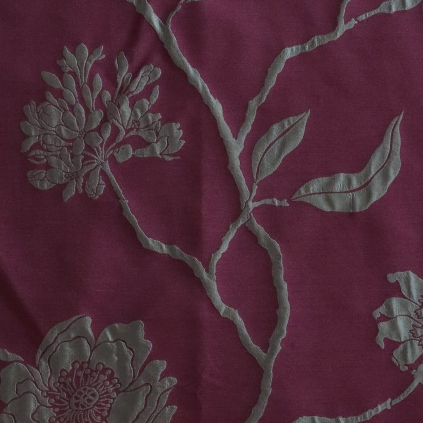 Close-up of PENCARROW RASPBERRY GOLD silk fabric from Arte Fresca Outlet, revealing the intricate details of its shimmering gold floral pattern with raised relief texture on a deep raspberry red background, emphasizing the luxurious silk weave.