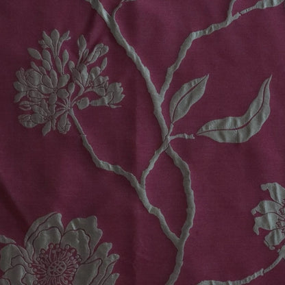 Close-up of PENCARROW RASPBERRY GOLD silk fabric from Arte Fresca Outlet, revealing the intricate details of its shimmering gold floral pattern with raised relief texture on a deep raspberry red background, emphasizing the luxurious silk weave.