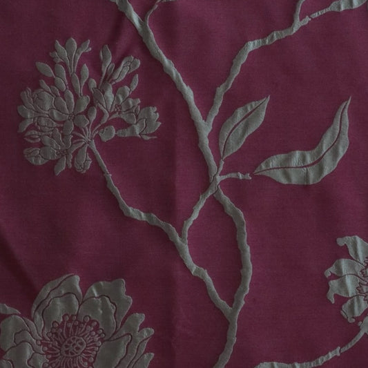 Close-up of PENCARROW RASPBERRY GOLD silk fabric from Arte Fresca Outlet, revealing the intricate details of its shimmering gold floral pattern with raised relief texture on a deep raspberry red background, emphasizing the luxurious silk weave.
