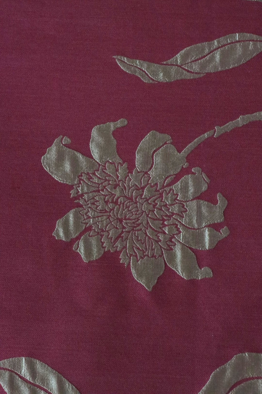 Close-up of PENCARROW RASPBERRY GOLD silk fabric from Arte Fresca Outlet, revealing the intricate details of its shimmering gold floral pattern with raised relief texture on a deep raspberry red background, emphasizing the luxurious silk weave.