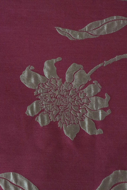 Close-up of PENCARROW RASPBERRY GOLD silk fabric from Arte Fresca Outlet, revealing the intricate details of its shimmering gold floral pattern with raised relief texture on a deep raspberry red background, emphasizing the luxurious silk weave.