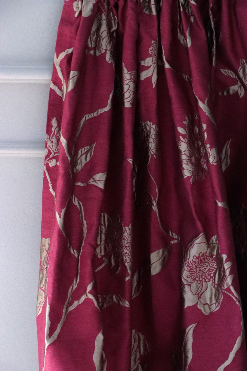 PENCARROW RASPBERRY GOLD silk fabric from Arte Fresca Outlet, elegantly folded in soft drapes like a curtain, showcasing its fluid quality, the luxurious gold floral pattern, and its suitability for opulent window treatments.