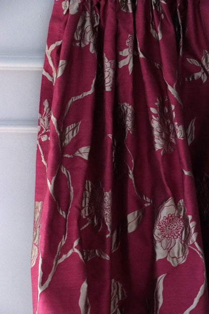 PENCARROW RASPBERRY GOLD silk fabric from Arte Fresca Outlet, elegantly folded in soft drapes like a curtain, showcasing its fluid quality, the luxurious gold floral pattern, and its suitability for opulent window treatments.