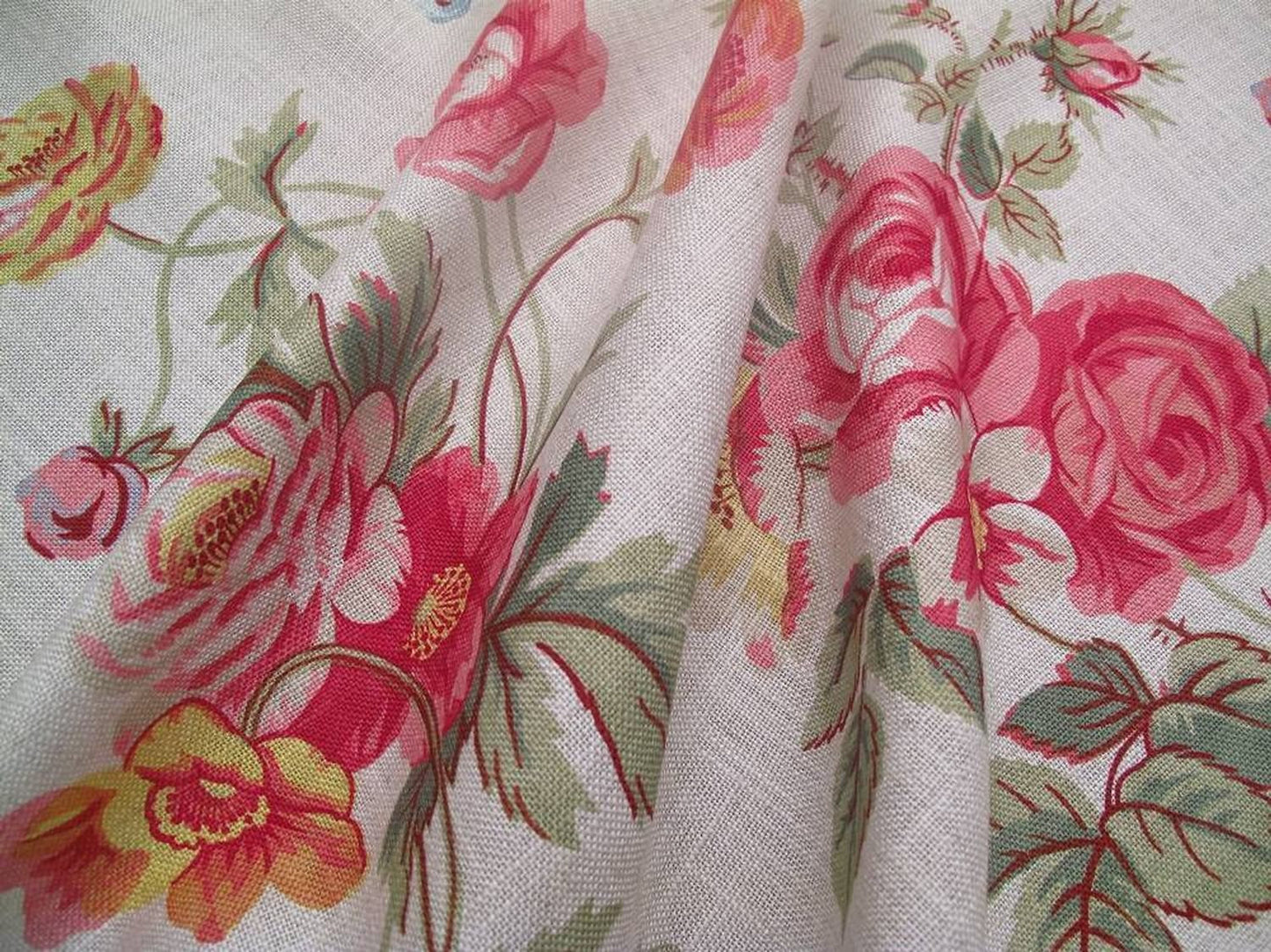Close-up of PHILIPPA PINK floral fabric from Arte Fresca Outlet, revealing the aquarelle-like detail of large crimson roses, small blue and yellow wildflowers, and red-veined green leaves on a textured off-white linen blend.