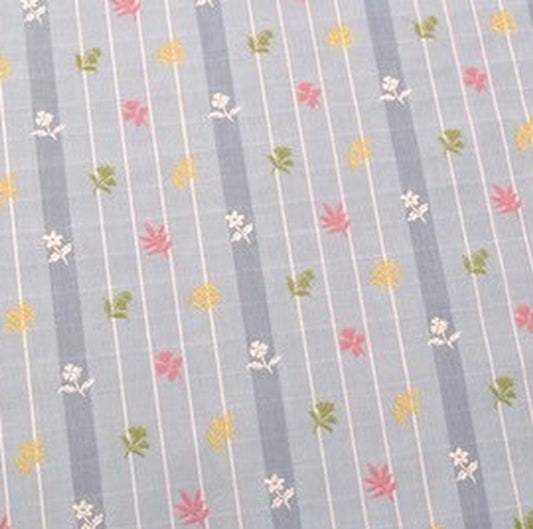 Close-up of SHIRLEY BLUE fabric from Arte Fresca Outlet, revealing the fine woven texture of the blue striped background, the intricate white grid, and the delicate raised embroidery of pink, yellow, and green floral motifs.