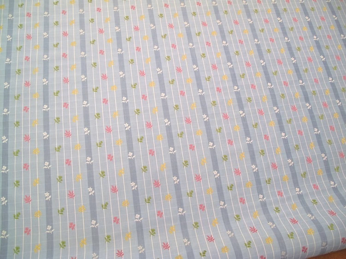 SHIRLEY BLUE fabric by Arte Fresca Outlet, a full view displaying its vertical blue stripes with white grid pattern and embroidered floral motifs in pink, yellow, and green, highlighting its charming English country style.