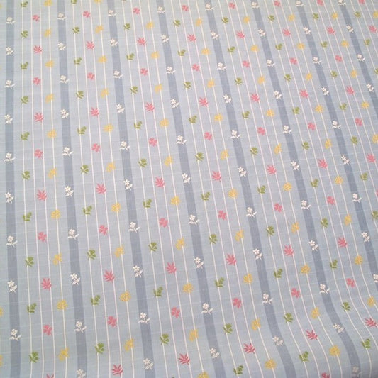 SHIRLEY BLUE fabric by Arte Fresca Outlet, a full view displaying its vertical blue stripes with white grid pattern and embroidered floral motifs in pink, yellow, and green, highlighting its charming English country style.
