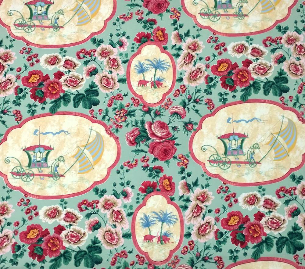 A repeating vintage floral pattern with pink and red roses on a light teal background, featuring cream-colored cartouches with illustrations of carriages, palm trees, and elephants.