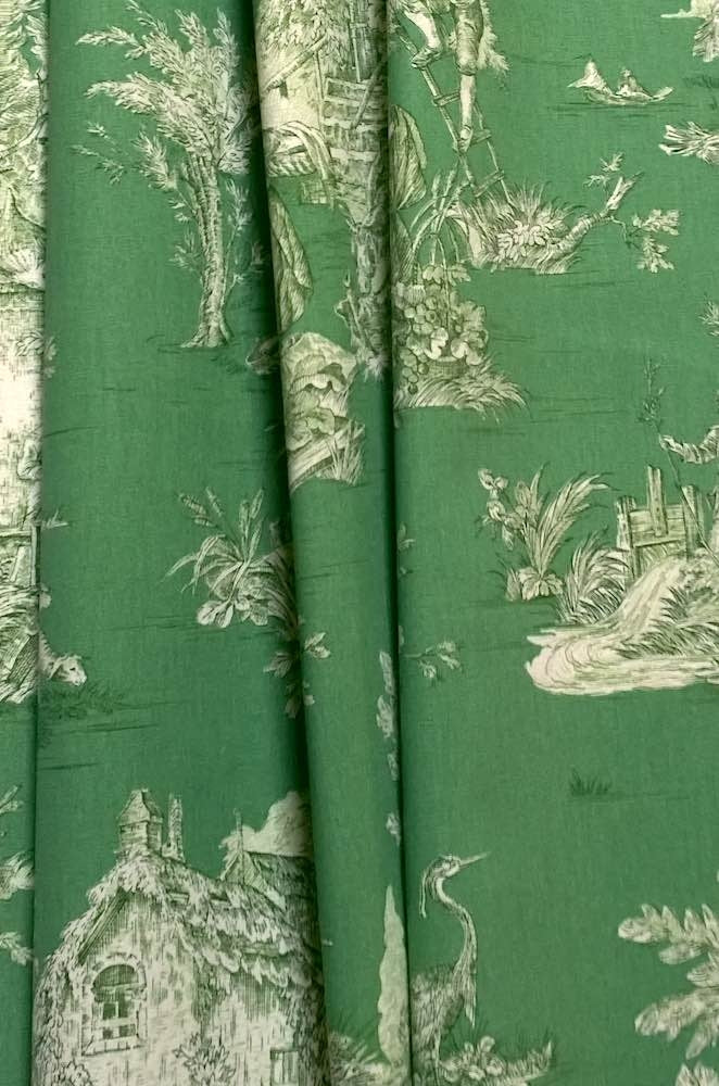 Green fabric with a classic white toile de Jouy pattern featuring houses, trees, birds, and figures in a scenic landscape.