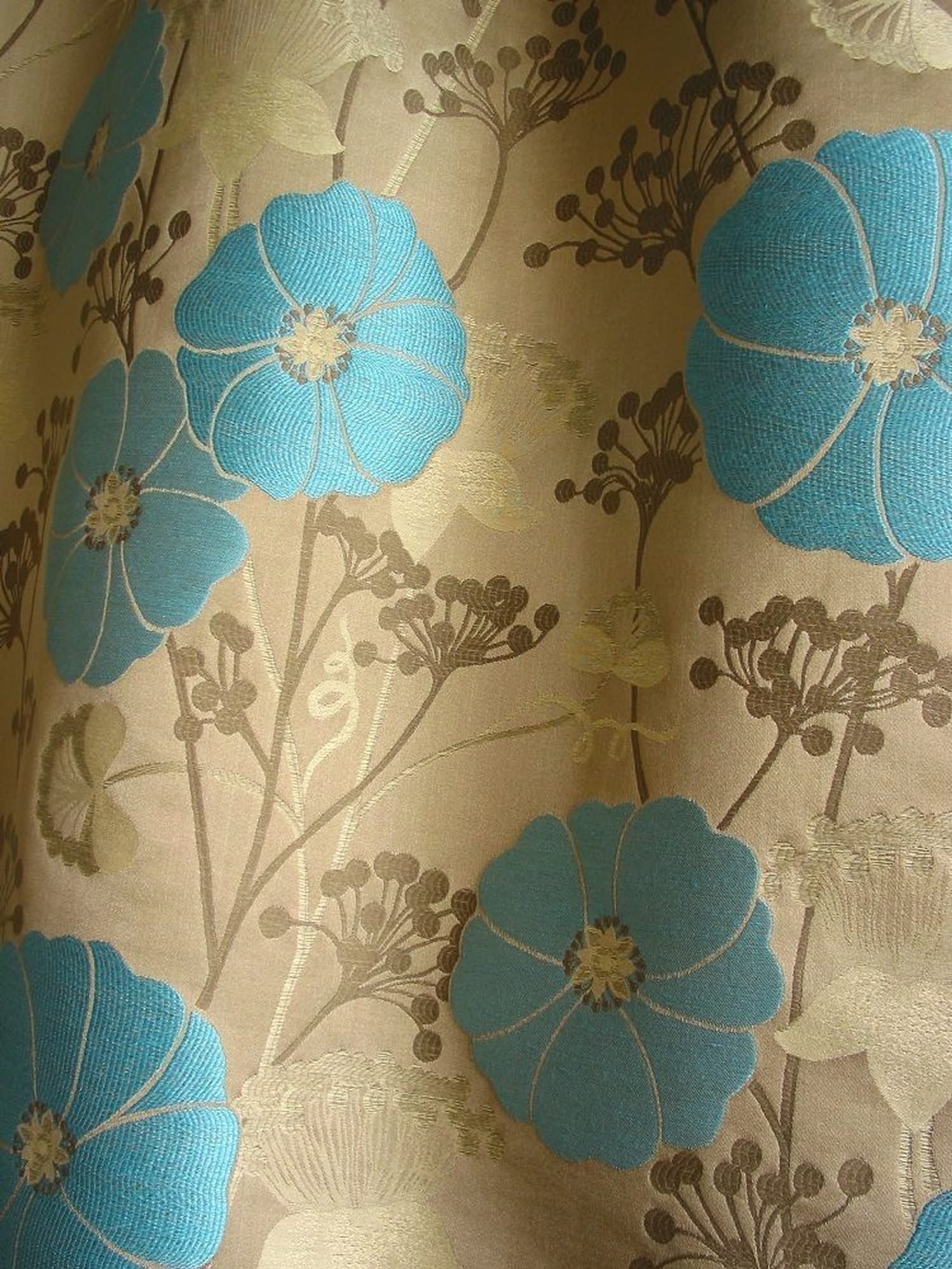 Close-up of VALENTIN TURQUOISE jacquard woven fabric from Arte Fresca Outlet, revealing the raised, textured turquoise-blue blossoms and intricate details of the floral pattern against the subtly shimmering beige background, showcasing the rich weave and blend of viscose, cotton, linen, and polyamide for upholstery and decor.