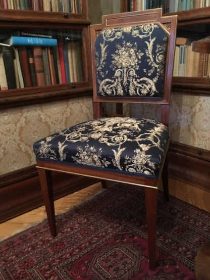 A collection of antique-style chairs and armchairs upholstered with the VILLA BORGHESE fabric in various colorways, including red and gold. The image shows the versatility of the elegant rococo pattern and its suitability for creating different moods within a classic interior design.