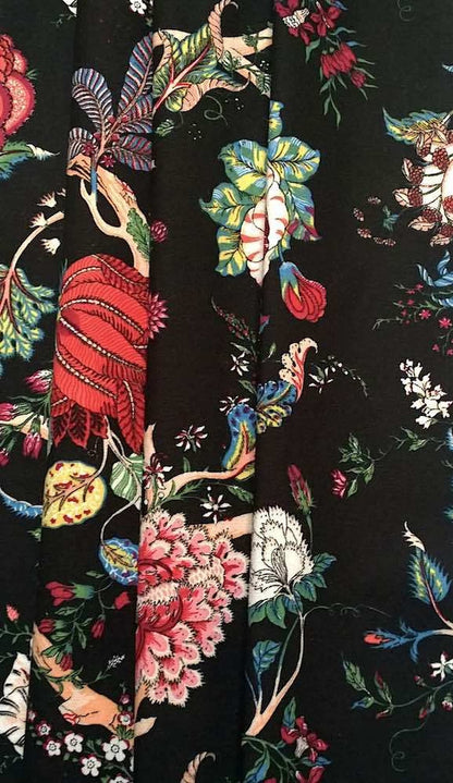 Villars Multi Black fabric coupon from Arte Fresca Outlet, folded like a curtain, displaying its beautiful drape and dramatic botanical design. The vibrant multi-colored blossoms on a deep black background of this smooth, printed 100% cotton fabric piece create an opulent and inviting look for window treatments.