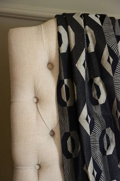 Voisin Black fabric by Arte Fresca Outlet draped loosely over a light upholstered chair, illustrating the scale of its repetitive geometric pattern for home decor inspiration.