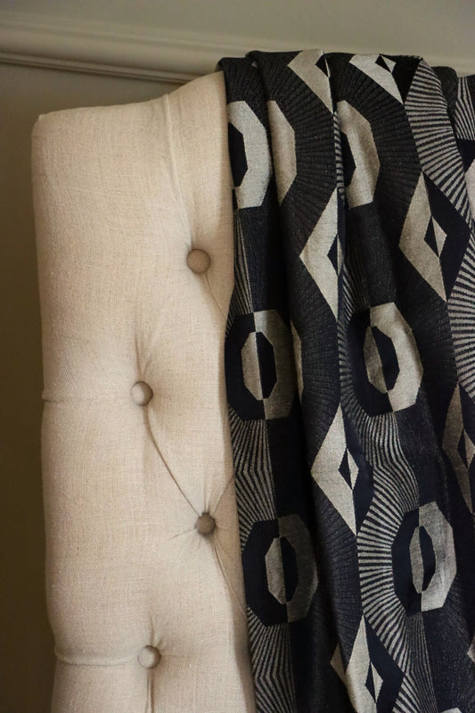 Voisin Black fabric by Arte Fresca Outlet draped loosely over a light upholstered chair, illustrating the scale of its repetitive geometric pattern for home decor inspiration.